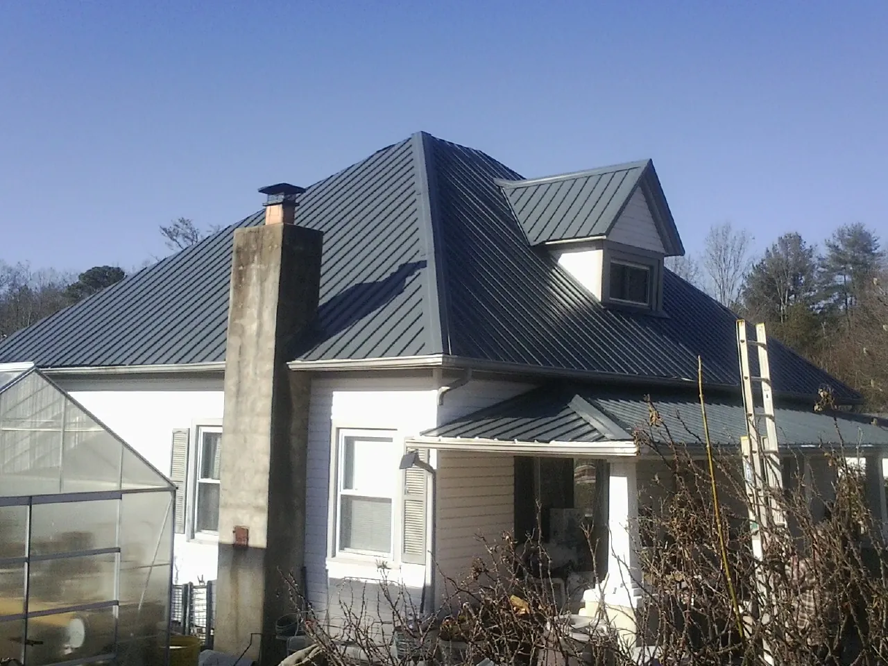 Dark blue standing seam metal roof on a white farmhouse with dormer — Slate & Tile Roof Repair by Roofing Brothers in Summit Lake
