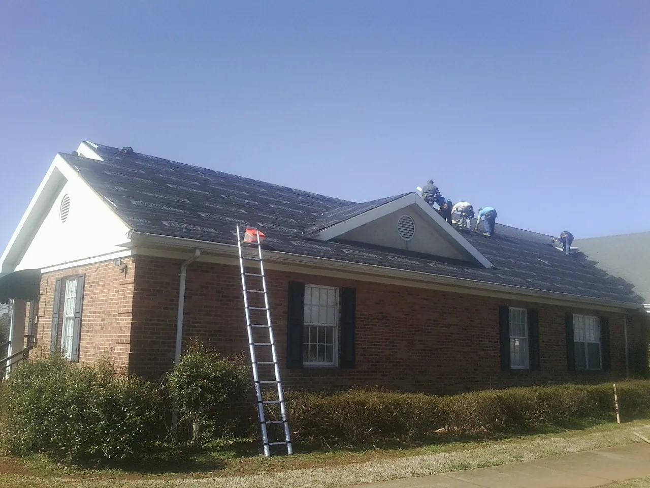 Crew tearing shingles off a brick ranch roof with a ladder set — Metal Roof Repair work by our crew in Summit Lake