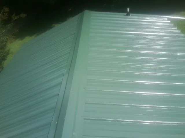 New green metal panels meeting at the ridge of a roof — Flat Roof Repair work by our crew in Summit Lake