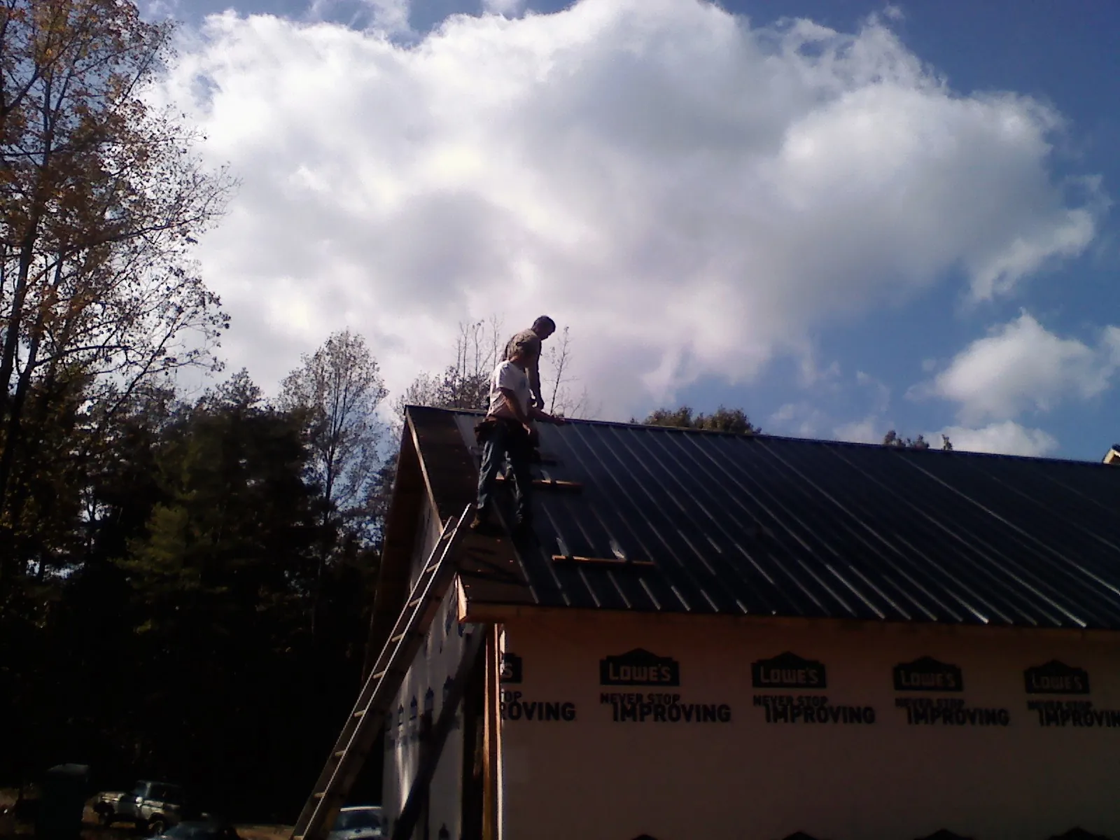 Roofer fastening dark metal panels high against a cloudy sky, from a Roof Inspection job in Summit Lake