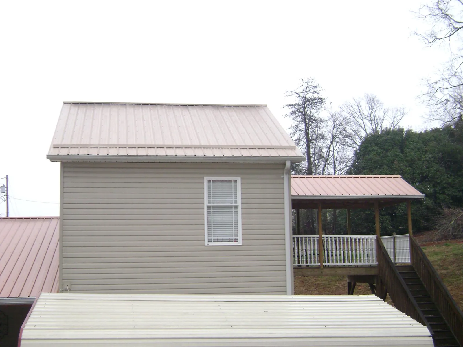 Tan metal roofs on a two story addition and attached porch, from a Roof Replacement job in Summit Lake